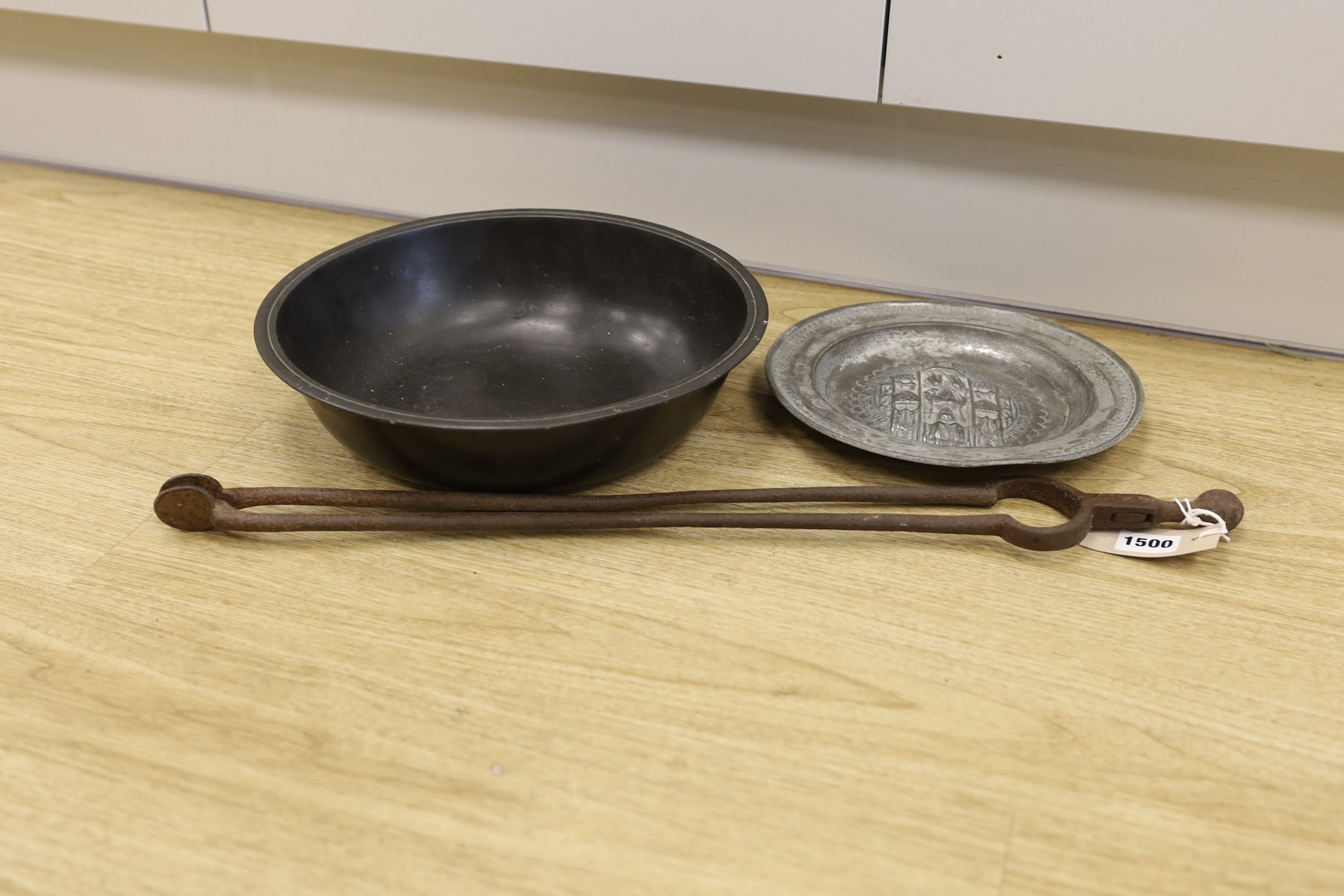 An 18th century pewter dish, an embossed pewter plate and a pair of iron fire tongs